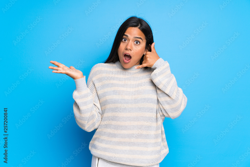 Young Colombian girl with sweater surprised and making phone gesture Young Colombian girl with sweater surprised and making phone gesture