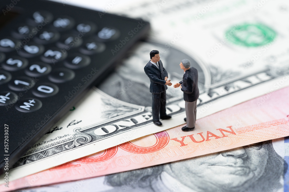 US and China finance economic direction, trade war, import and export deal and agreement concept, calculator with miniature leader hand shaking on US dollar and china yuan banknotes, tariff situation US and China finance economic direction, trade war, import and export deal and agreement concept, calculator with miniature leader hand shaking on US dollar and china yuan banknotes, tariff situation