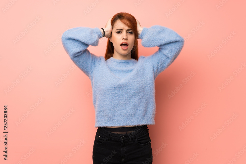 Young redhead woman over pink background takes hands on head because has migraine Young redhead woman over pink background takes hands on head because has migraine