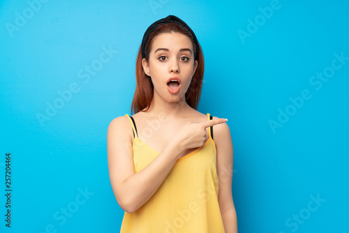 Young redhead woman over blue background surprised and pointing side