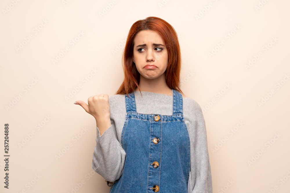 Young redhead woman over isolated background unhappy and pointing to the side Young redhead woman over isolated background unhappy and pointing to the side