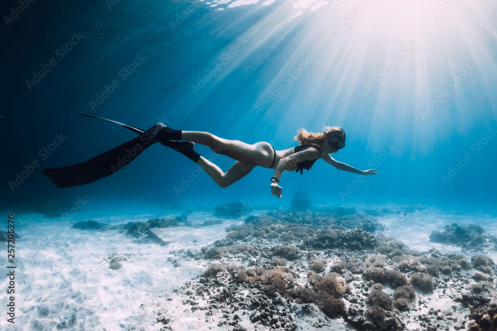 Woman freediver with fins swim over sandy sea and sun rays. Underwater ocean
