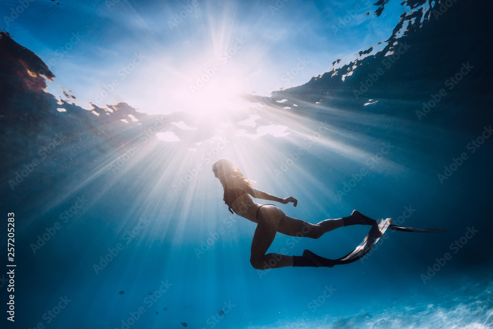 Woman freediver with fins swim over sandy bottom and sun rays underwater ocean