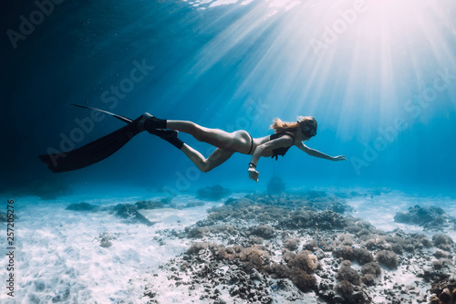 Woman freediver with fins swim over sandy sea and sun rays. Underwater ocean