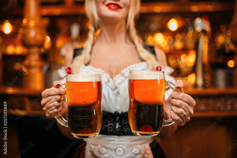 Sexy waitress holds two mugs of fresh beer in pub