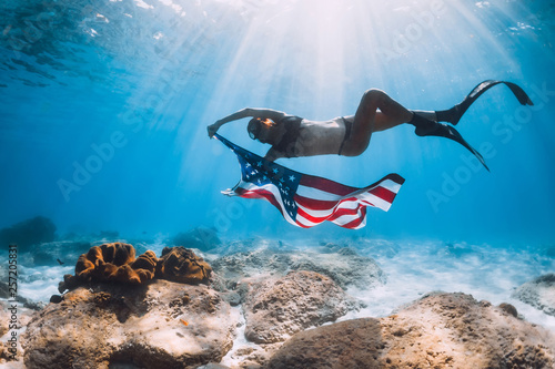 Woman freediver swim over sandy sea bottom with USA flag. Independence day