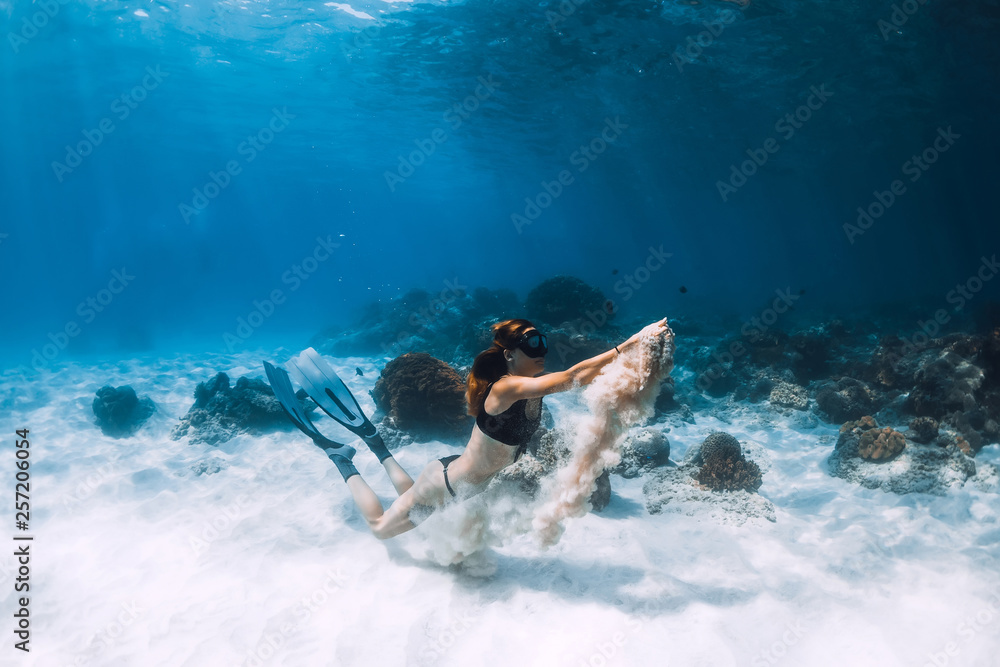 Woman freediver with fins swim over sandy bottom and sun rays underwater ocean