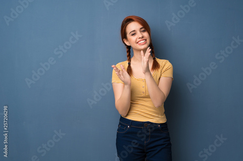 Young redhead woman over blue background applauding after presentation in a conference © luismolinero