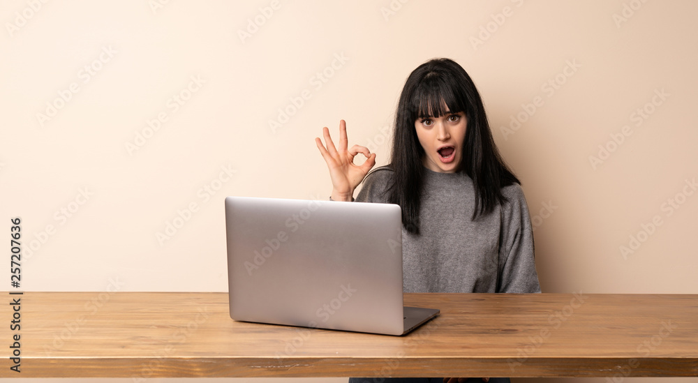 Young woman working with her laptop surprised and showing ok sign Young woman working with her laptop surprised and showing ok sign