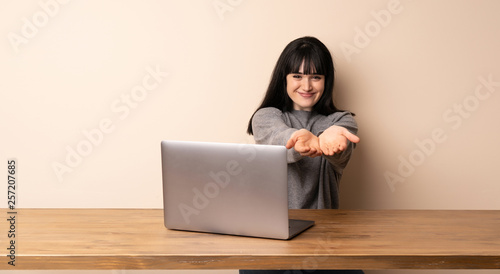 Young woman working with her laptop holding copyspace imaginary on the palm to insert an ad