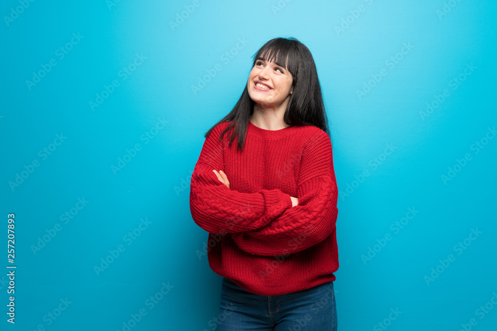 Woman with red sweater over blue wall looking up while smiling Woman with red sweater over blue wall looking up while smiling