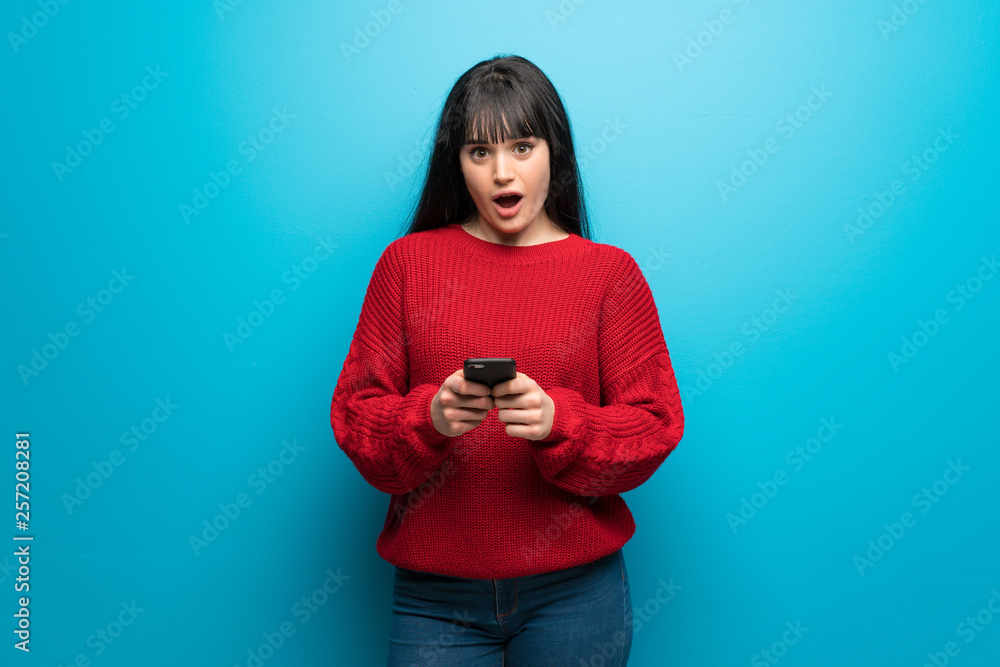 Woman with red sweater over blue wall surprised and sending a message Woman with red sweater over blue wall surprised and sending a message