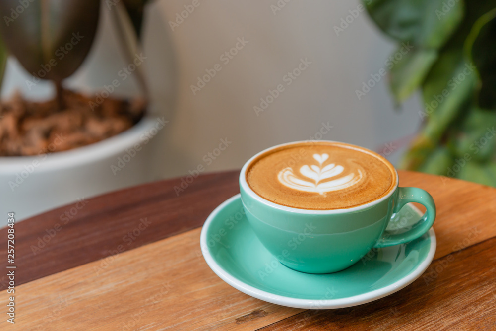 Hot cappuccino coffee in a green cup with latte art on the wooden table in the coffee shop. Hot cappuccino coffee in a green cup with latte art on the wooden table in the coffee shop.