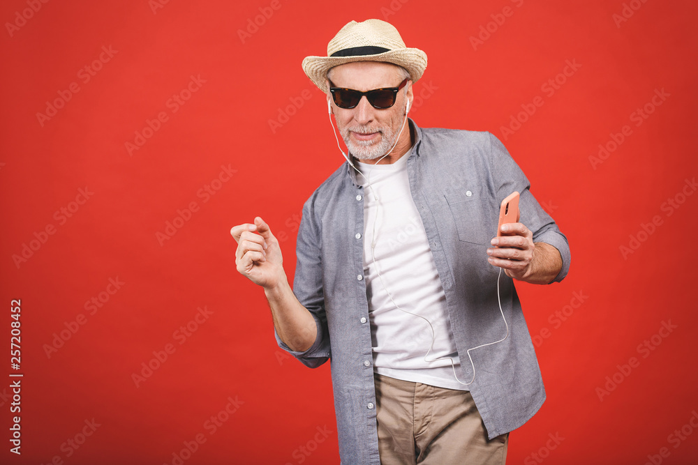 Portrait of senior happy cheerful elderly man dancing and listening music witn phone and headphones isolated against red background. Portrait of senior happy cheerful elderly man dancing and listening music witn phone and headphones isolated against red background.
