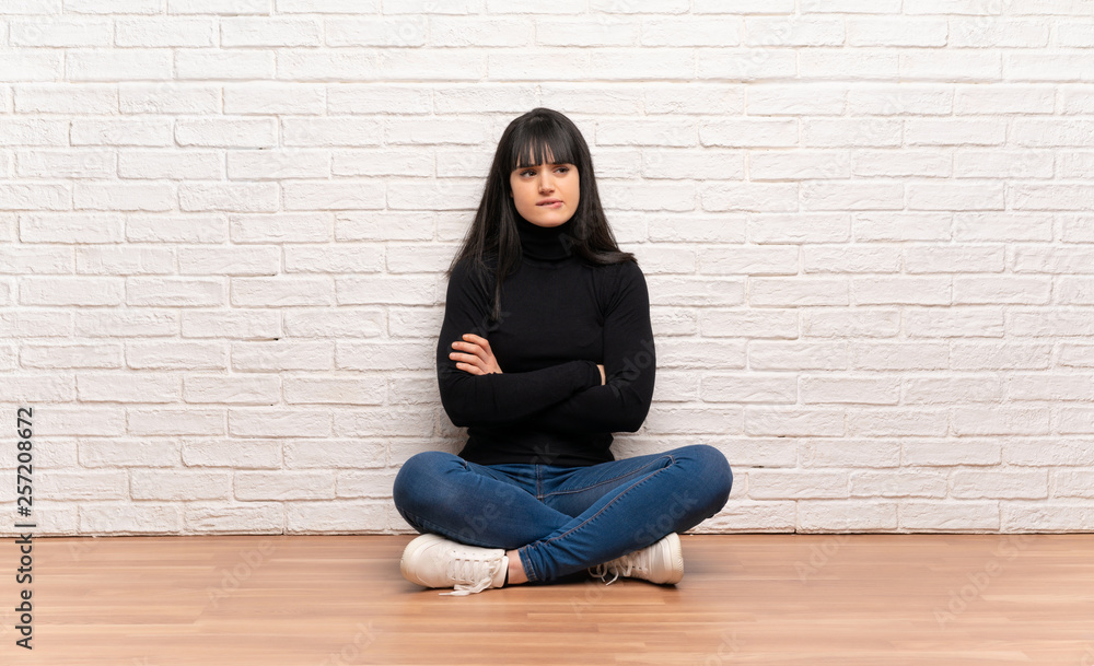 Woman sitting on the floor with confuse face expression while bites lip Woman sitting on the floor with confuse face expression while bites lip