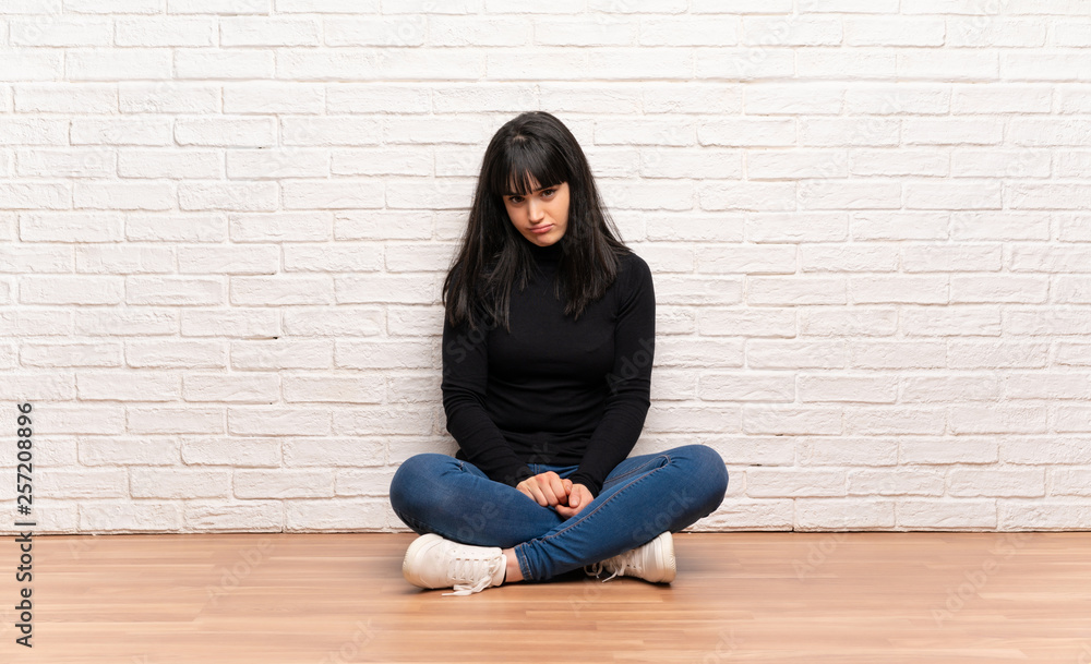 Woman sitting on the floor with sad and depressed expression Woman sitting on the floor with sad and depressed expression