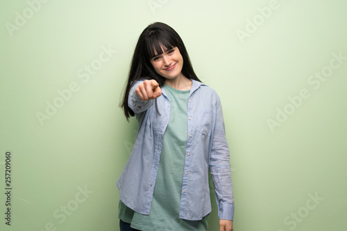 Young woman over green wall points finger at you with a confident expression © luismolinero