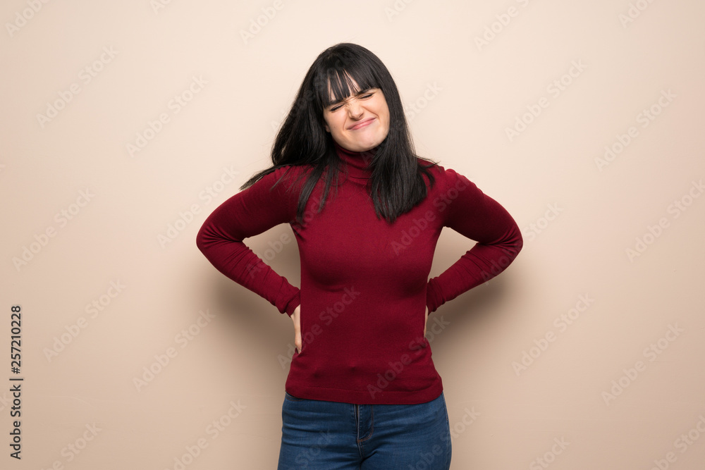 Young woman with red turtleneck suffering from backache for having made an effort Young woman with red turtleneck suffering from backache for having made an effort