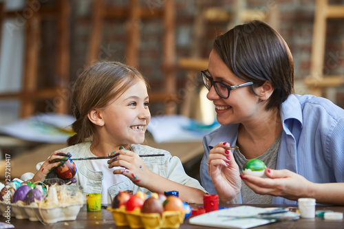Wall Mural Portrait of happy little girl painting easter eggs with mothera nd looking at ea