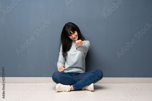Woman sitting on the floor inviting to come with hand. Happy that you came