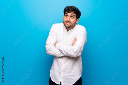 Young man over isolated blue wall making doubts gesture while lifting the shoulders