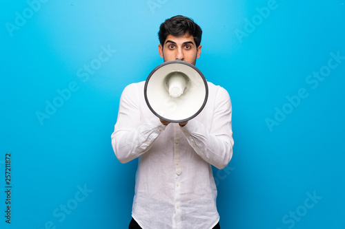 Young man over isolated blue wall shouting through a megaphone