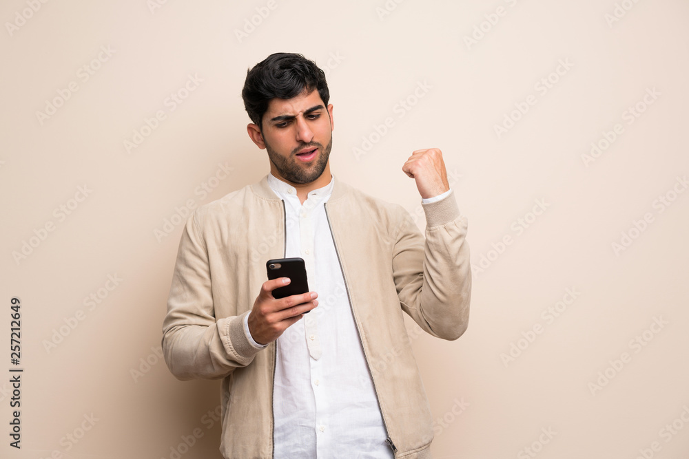 Young man over isolated wall with phone in victory position Young man over isolated wall with phone in victory position
