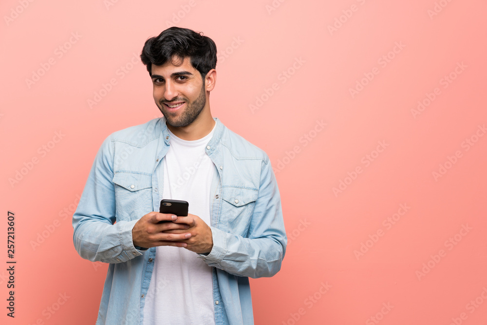 Young man over pink wall sending a message with the mobile Young man over pink wall sending a message with the mobile