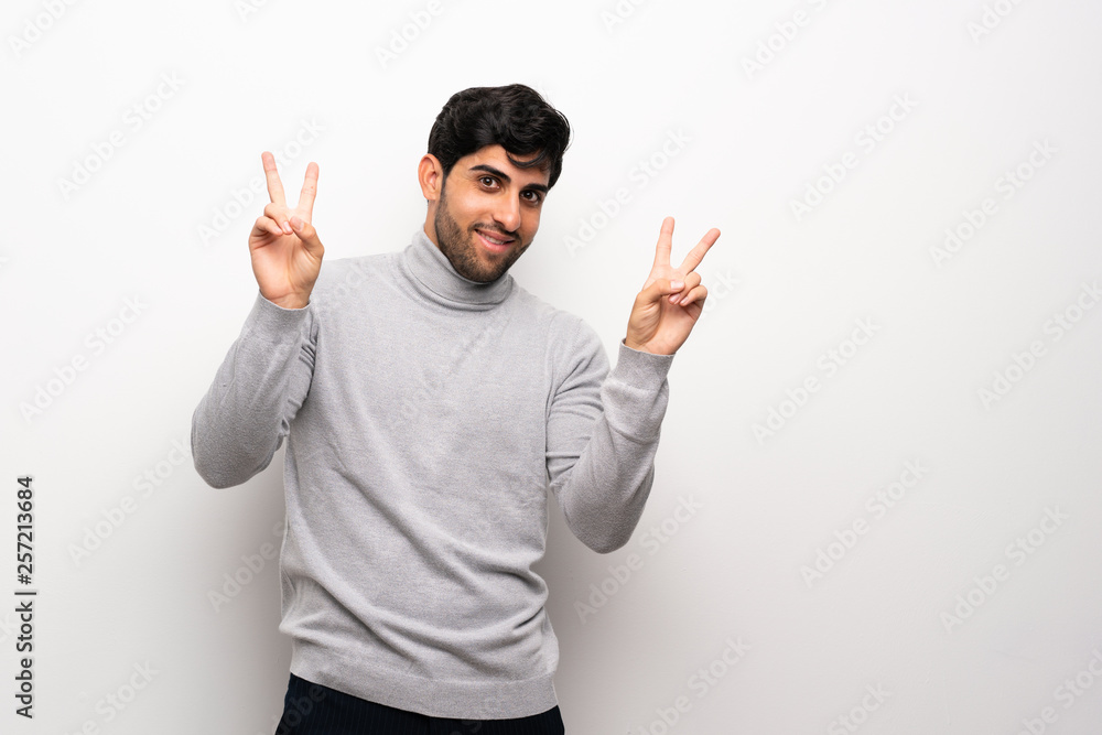 Young man over isolated white wall showing victory sign with both hands Young man over isolated white wall showing victory sign with both hands