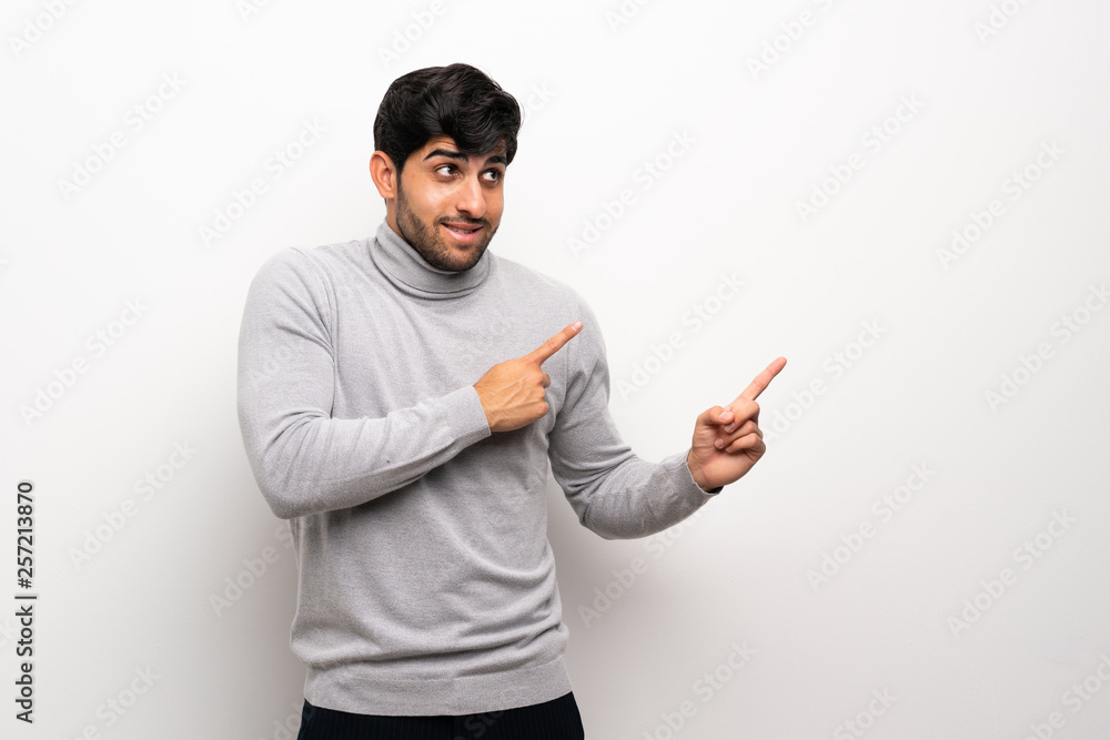 Young man over isolated white wall frightened and pointing to the side Young man over isolated white wall frightened and pointing to the side