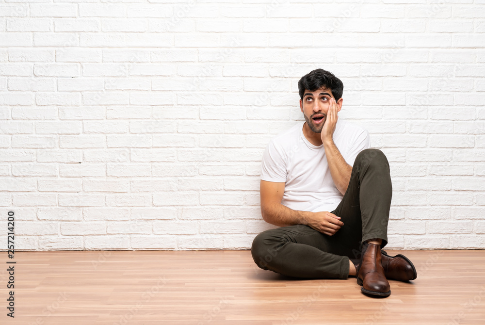 Young man sitting on the floor with surprise and shocked facial expression Young man sitting on the floor with surprise and shocked facial expression