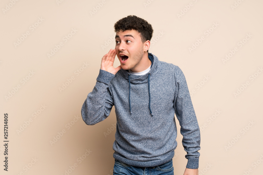 Young man over isolated wall shouting with mouth wide open to the lateral Young man over isolated wall shouting with mouth wide open to the lateral