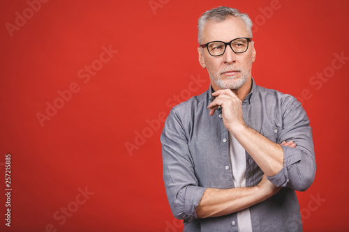 Portrait of a mature serious businessman wearing glasses isolated against red background. Happy senior man looking at camera with copy space. 