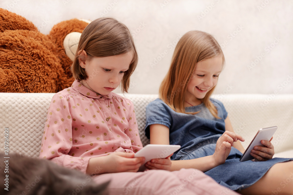 Two little girls (sisters 7 and 8 years old) are watching an e-book and a smartphone at home on the sofa with their cat. Two little girls (sisters 7 and 8 years old) are watching an e-book and a smartphone at home on the sofa with their cat.