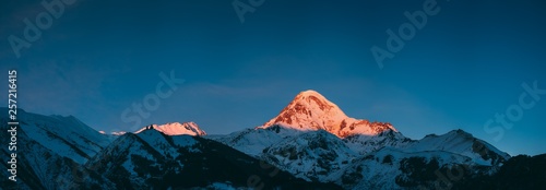 Georgia. Mount Kazbek Covered Snow In Winter Sunrise. Morning Dawn Colored Top Of Mountain In Pink-orange Colors. Awesome Winter Georgian Nature Landscape.