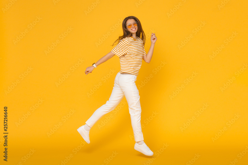 Cheerful positive girl jumping in the air, isolated on yellow background
