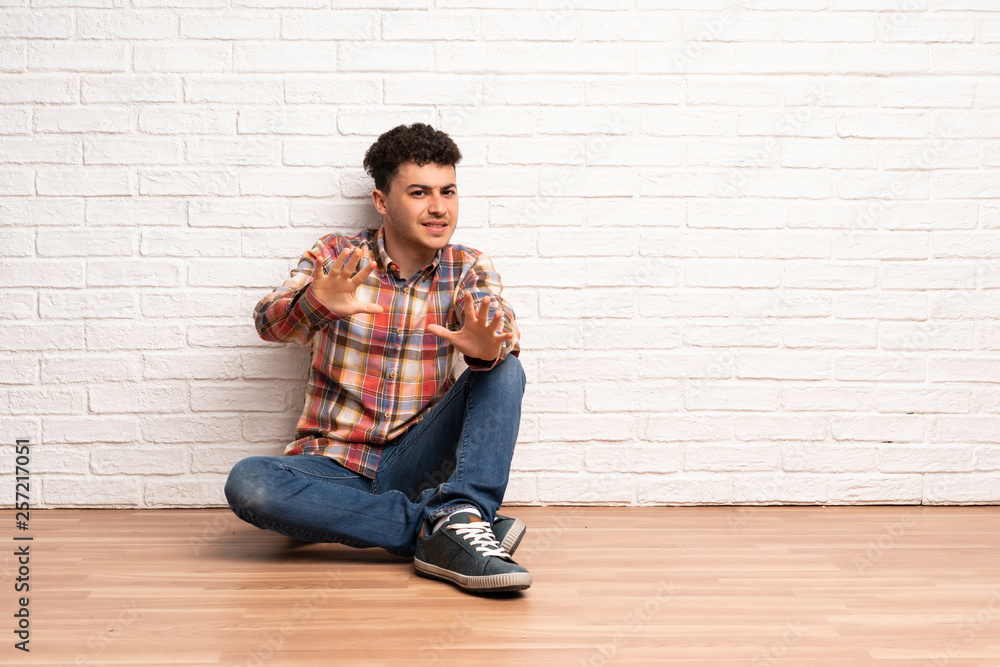 Young man sitting on the floor nervous stretching hands to the front Young man sitting on the floor nervous stretching hands to the front