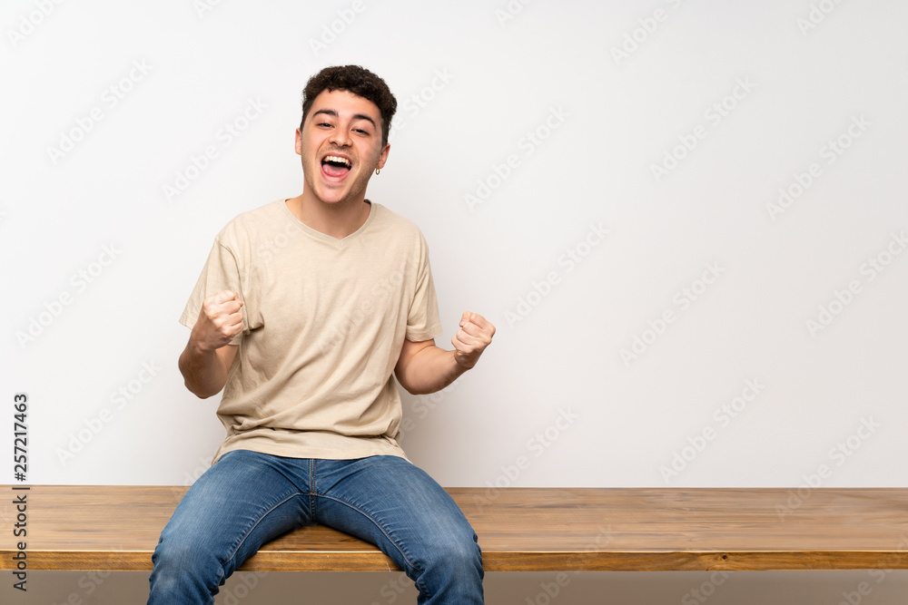 Fototapeta premium Young man sitting on table celebrating a victory in winner position