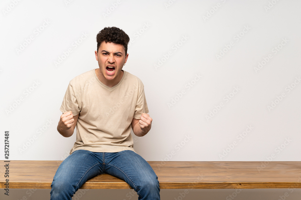 Young man sitting on table frustrated by a bad situation Young man sitting on table frustrated by a bad situation