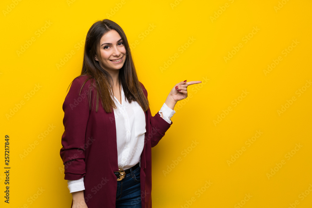 Young woman over yellow wall pointing finger to the side Young woman over yellow wall pointing finger to the side
