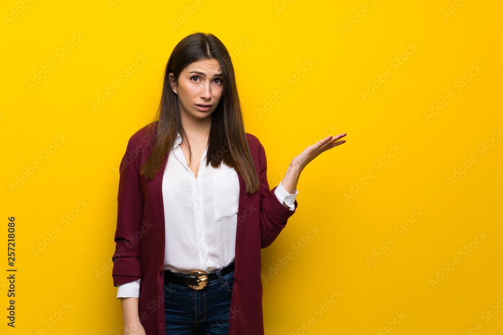 Young woman over yellow wall making doubts gesture Young woman over yellow wall making doubts gesture