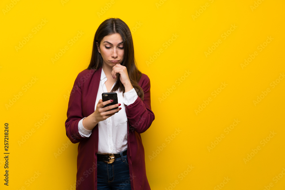 Young woman over yellow wall thinking and sending a message Young woman over yellow wall thinking and sending a message
