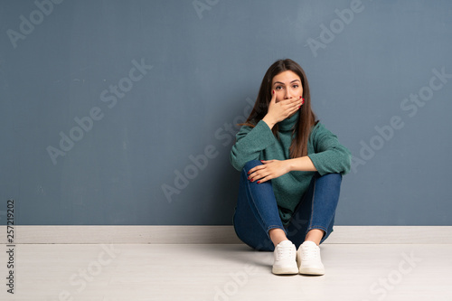 Young woman sitting on the floor covering mouth with hands for saying something inappropriate © luismolinero