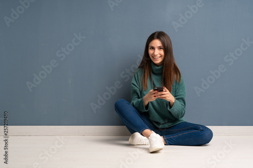 Young woman sitting on the floor sending a message with the mobile