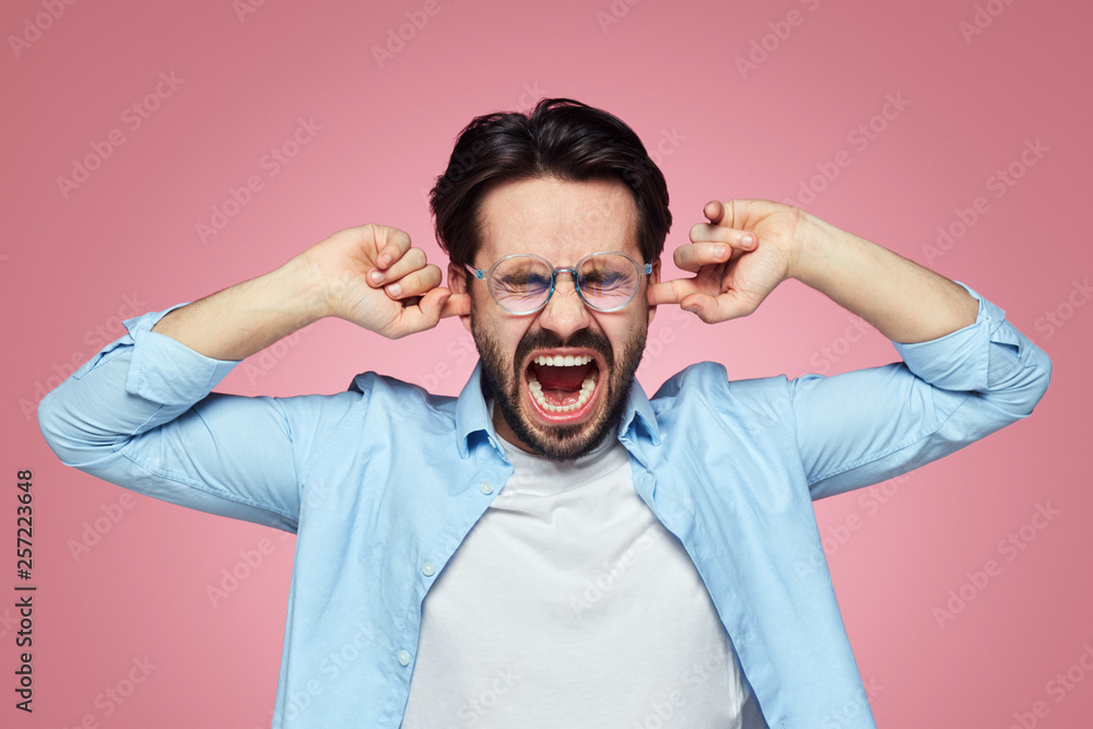 Irritated handsome male plugs ears and screaming to ignore a conflict