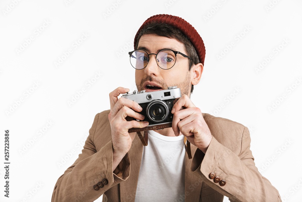 Photo of positive man 30s wearing hipster hat rejoicing while holding and photographing on retro camera Photo of positive man 30s wearing hipster hat rejoicing while holding and photographing on retro camera