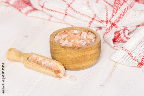 Lot of pieces of mineral pink himalayan salt crystals in a wooden bowl on white wood