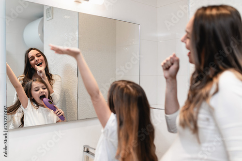 Pregnant woman and her cute little daughter having fun in bathroom while they combing hair.
