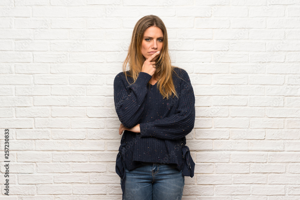 Blonde woman over brick wall having doubts and thinking Blonde woman over brick wall having doubts and thinking