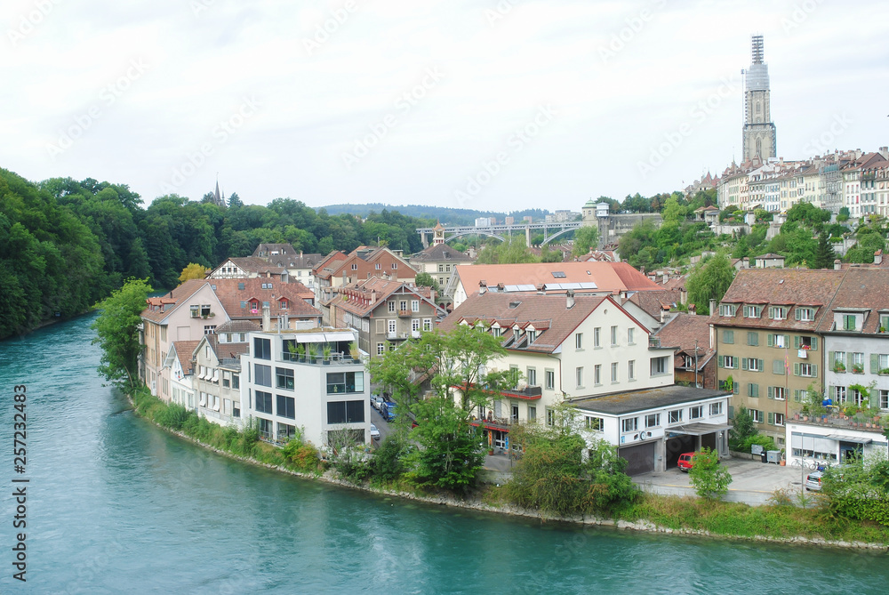 A cityscape view old town of Bern, the capital of Switzerland in overcast day. The city is crowded with houses and buildings, mountain, bridge and river background